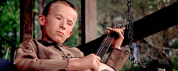 Another boy is playing the fret from behind, which explains the angle. The camera angle also elevates the boy into a position of authority. He knows something the men do not.