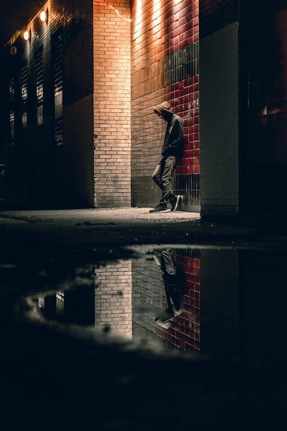 man in hoodie at night with his reflection in puddle